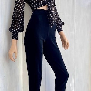 Puede incluir: Un atuendo negro que consta de una blusa de lunares y pantalones de cintura alta. La blusa tiene mangas largas y un lazo en la cintura. Los pantalones son cortos y tienen un corte entallado. El atuendo se muestra en un maniquí.