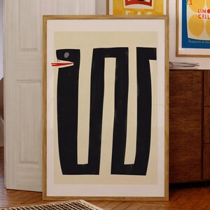 May include: A framed abstract art print with a black and white design of a snake with a red mouth. The background is a light beige color.