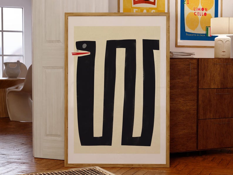 May include: A framed abstract art print with a black and white design of a snake with a red mouth. The background is a light beige color.