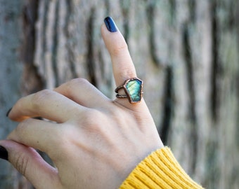 May include: A copper ring with a green and blue labradorite stone set in a coffin shape.