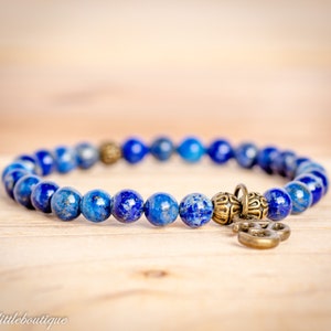 May include: A blue lapis lazuli beaded bracelet with a gold-toned charm. The bracelet is made with small, round beads and has a simple design.