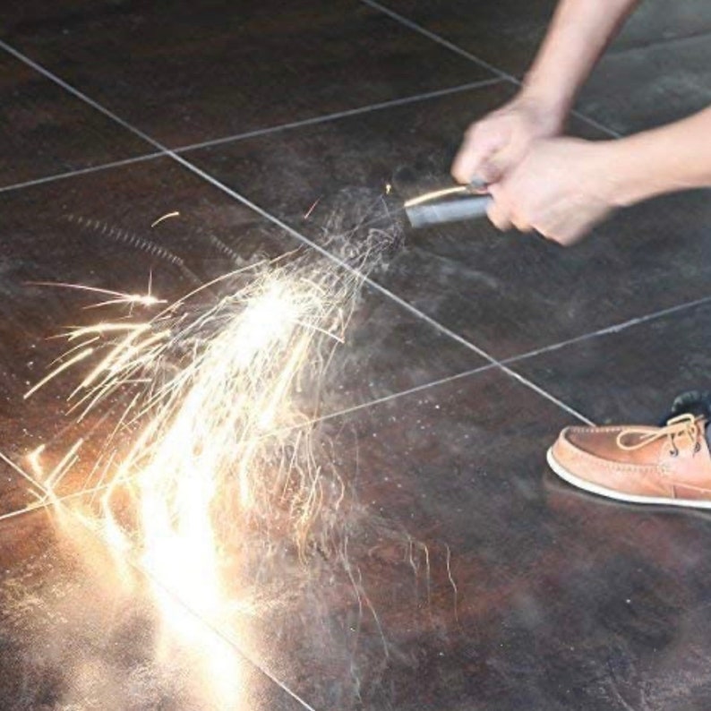 Puede incluir: Una persona est&aacute; usando un iniciador de fuego para crear chispas en un suelo de baldosas. Las chispas salen volando del iniciador de fuego en un color blanco y amarillo brillante.
