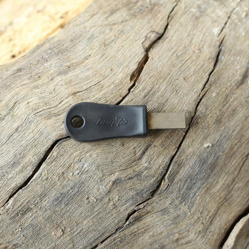 Puede incluir: Un encendedor de fuego negro con un mango y un percutor de metal. El mango tiene un agujero para sujetar un cord&oacute;n y el texto "Light My Fire" est&aacute; impreso en el mango.