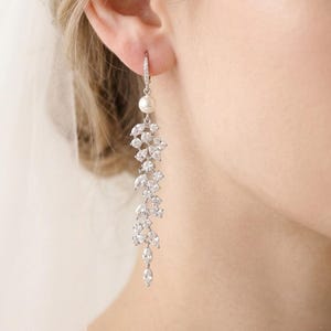 May include: Silver-tone drop earrings with a pearl and clear crystal cascade. The earrings have a floral design with multiple crystal shapes. Ideal for formal events, these earrings are a sophisticated accessory.