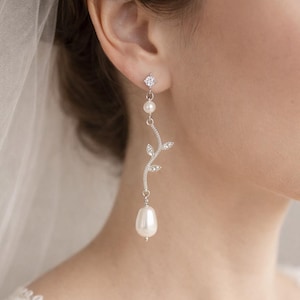 May include: Silver drop earrings with a sparkling round stud, a small pearl, and a delicate vine design with clear crystals. The earrings end with a large, teardrop-shaped pearl. Ideal for bridal or special occasion wear.