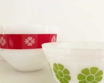 May include: Two white ceramic mixing bowls with different patterns. One bowl has a red band with white floral designs. The other bowl has green floral designs.