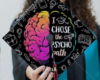 May include: Black graduation cap with a colorful brain graphic and the text "I CHOSE the PSYCHO path." The design includes academic icons and a red tassel. The cap is held by a person.