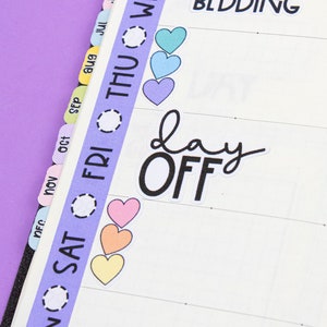 Puede incluir: Primer plano de un planificador con pestañas de colores para cada mes del año. El planificador tiene un diseño semanal con pegatinas que dicen "change bedding" y "day off".