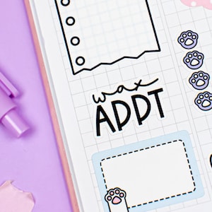 May include: A pink and white planner with a grid pattern. The planner has a sticker that says "wax appt" and a paw print sticker. There is a pen and a piece of tape on the planner.