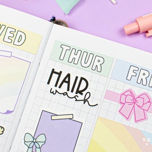 May include: A weekly planner with colorful stickers. The stickers include a rainbow, a bow, a girl with a gift, and a sticker that says "HAIR wash".