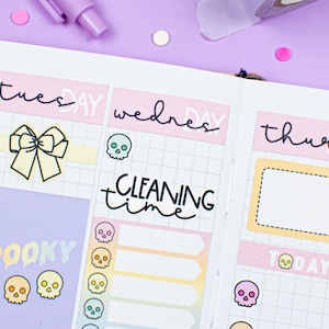 Puede incluir: Un planificador semanal con un esquema de color rosa, amarillo y blanco. El planificador tiene un diseño de cuadrícula con los días de la semana etiquetados como "Martes", "Miércoles" y "Jueves". El planificador incluye pegatinas con un lazo, calaveras y el texto "Tiempo de limpieza" y "Spooky".