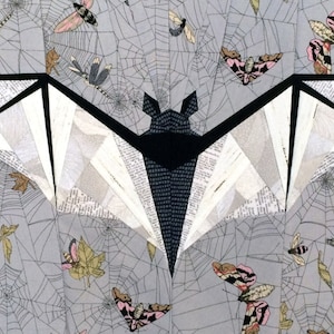 Può includere: Un pipistrello di carta bianco e nero su uno sfondo grigio. Il pipistrello è fatto di carta e ha un design geometrico. Lo sfondo è ricoperto da un motivo di ragnatele grigie e piccole farfalle rosa e bianche.