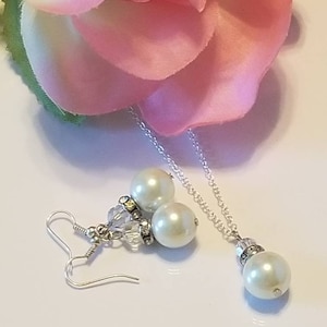 May include: A pearl necklace and earrings set with a silver chain and white pearls. The necklace has a single pearl pendant and the earrings have two pearls each.