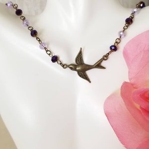 May include: A delicate necklace with a bronze bird pendant and purple and lavender crystal beads.