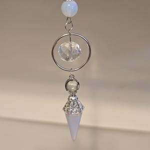 May include: A silver and white crystal pendulum with a clear crystal charm and a white opal bead.