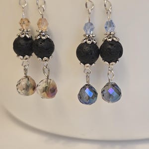 May include: A pair of silver earrings with black lava rock beads and crystal accents. The earrings have a dangling design with a smaller crystal bead at the bottom.