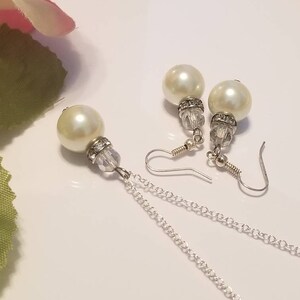 May include: A set of pearl earrings and a pearl necklace with a silver chain. The earrings feature a crystal bead and a pearl drop. The necklace has a single pearl drop and a silver chain.