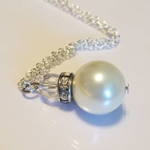 May include: A silver chain necklace with a large white pearl pendant. The pearl is accented with a clear crystal bead and rhinestones.