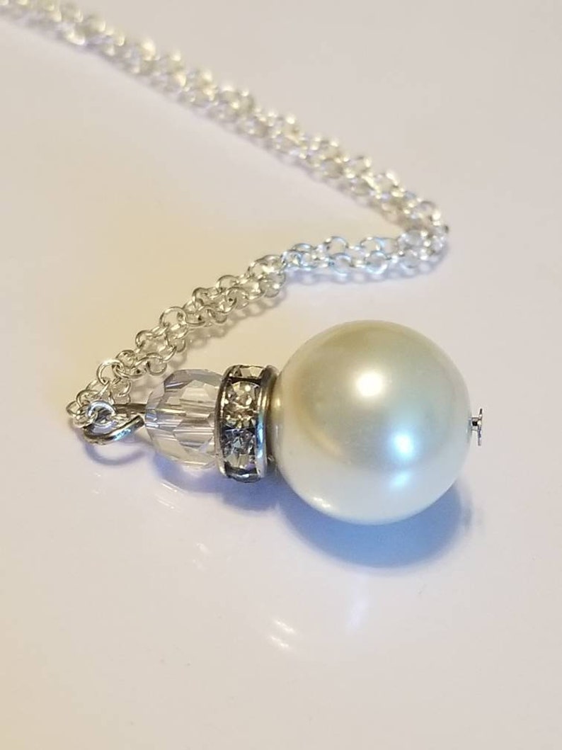 May include: A silver chain necklace with a large white pearl pendant. The pearl is accented with a clear crystal bead and rhinestones.