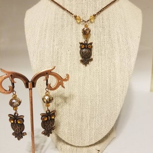 May include: A copper owl necklace and earrings set with amber glass beads. The owl pendant and earrings feature detailed wings and eyes.