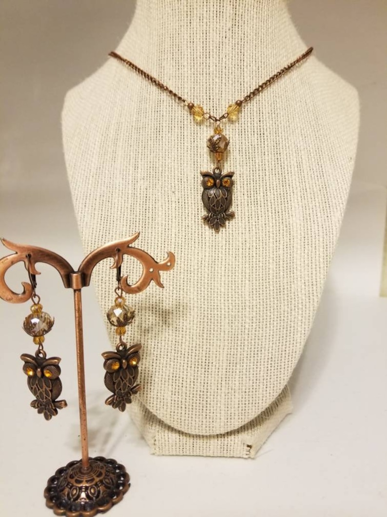 May include: A copper owl necklace and earrings set with amber glass beads. The owl pendant and earrings feature detailed wings and eyes.