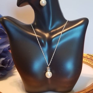 May include: A silver necklace and earrings set with a pearl and crystal pendant. The necklace has a delicate silver chain and the earrings are drop style.