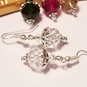May include: A pair of silver dangle earrings with clear crystal teardrop shaped beads. The beads have a faceted design and are accented with silver filigree.