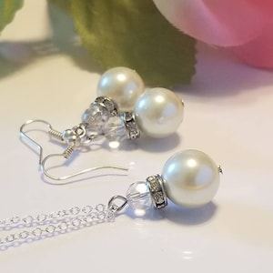May include: A silver chain necklace with a crystal pendant and a large white pearl. Matching earrings with a crystal and a smaller white pearl.