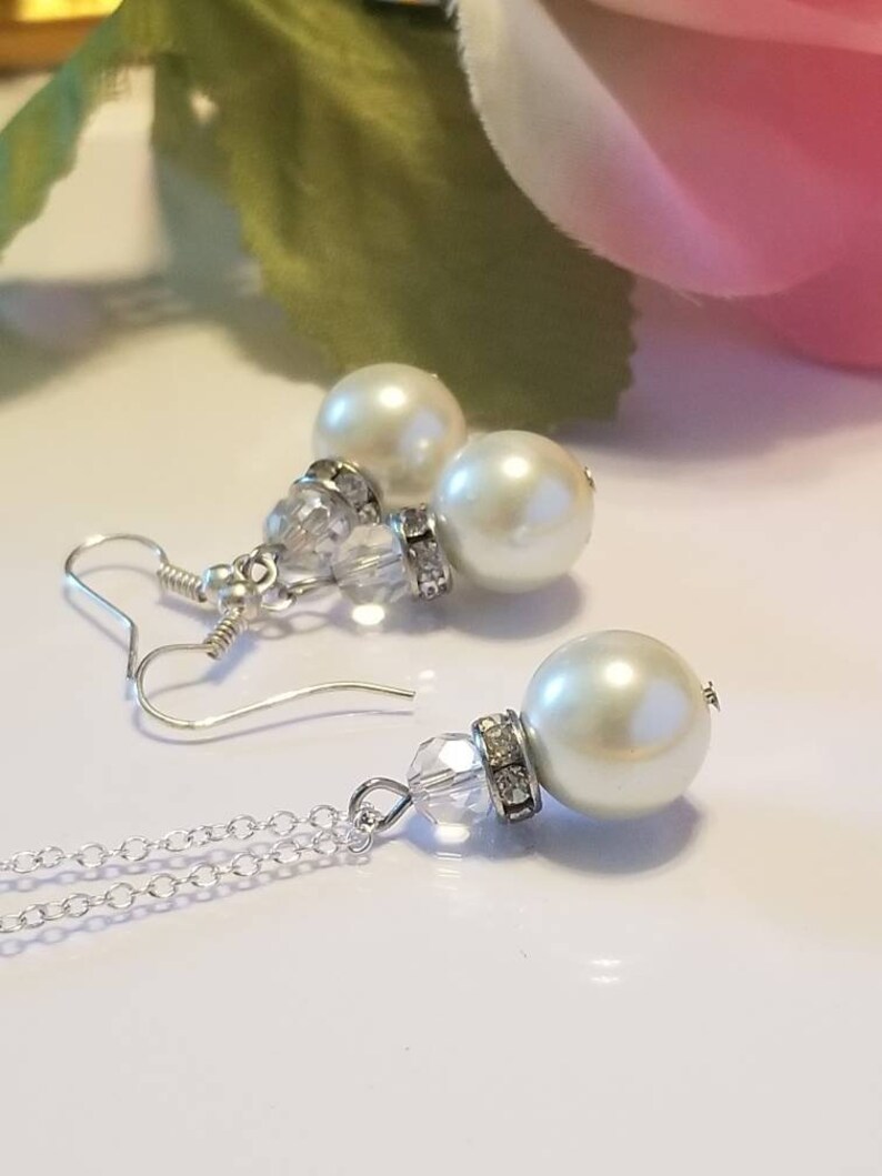 May include: A silver chain necklace with a crystal pendant and a large white pearl. Matching earrings with a crystal and a smaller white pearl.