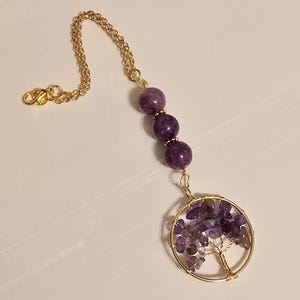 May include: A gold chain necklace with a purple amethyst tree of life pendant. The pendant is made of wire wrapped around small amethyst stones.