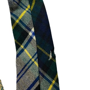Pode incluir: Um close-up de um tecido xadrez verde, azul e amarelo com uma borda desfiada. O tecido est&aacute; dobrado sobre si mesmo, criando uma linha diagonal.