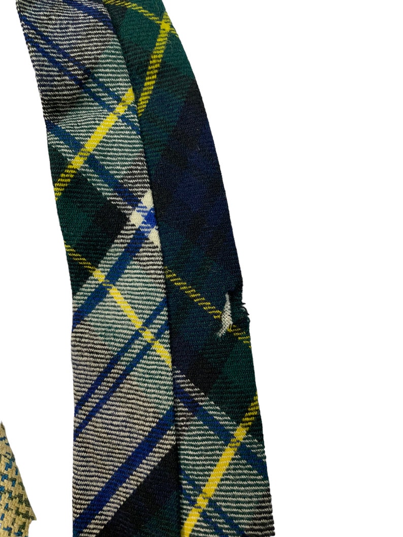 Pode incluir: Um close-up de um tecido xadrez verde, azul e amarelo com uma borda desfiada. O tecido est&aacute; dobrado sobre si mesmo, criando uma linha diagonal.