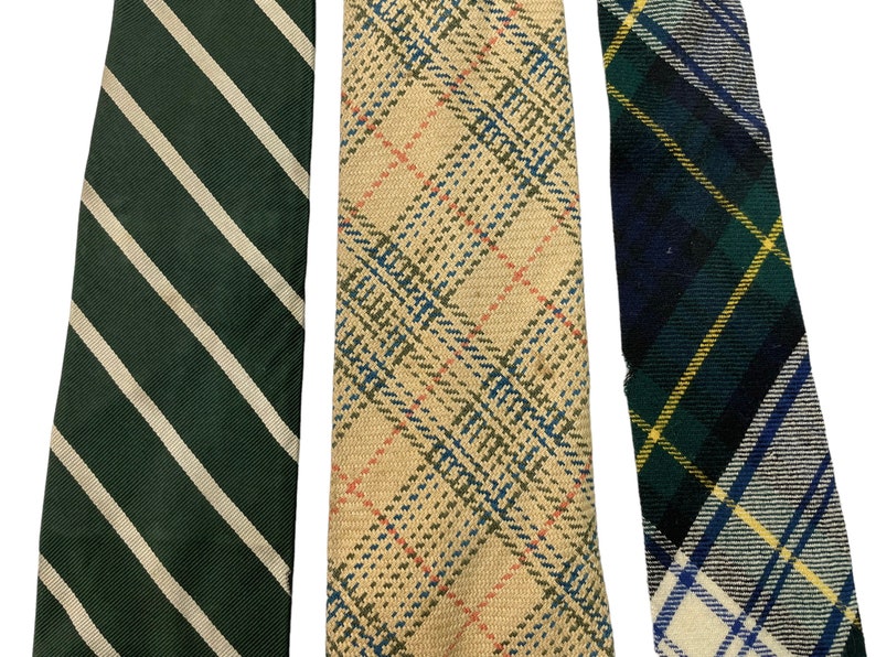 Pode incluir: Tr&ecirc;s gravatas com padr&otilde;es diferentes. A primeira gravata &eacute; verde com listras brancas. A segunda gravata &eacute; bege com um padr&atilde;o xadrez vermelho, azul e branco. A terceira gravata &eacute; xadrez azul, verde e branco.