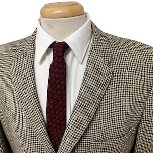 Può includere: Blazer in tweed con classico motivo a pied-de-poule nei toni del marrone, nero e beige. Il blazer è abbinato a una camicia bianca e a una cravatta bordeaux a fantasia paisley. La giacca ha un revers a lancia e una chiusura a due bottoni.