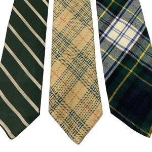 Pode incluir: Tr&ecirc;s gravatas com padr&otilde;es diferentes. A primeira gravata &eacute; verde com listras brancas. A segunda gravata &eacute; bege com um padr&atilde;o xadrez vermelho e azul. A terceira gravata &eacute; xadrez verde, azul e amarelo.