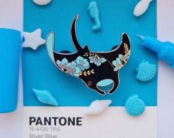 May include: A black and blue enamel pin of a manta ray with floral details. The pin is on a blue background with white and blue accents. PANTONE 15-4720 TPG River Blue.