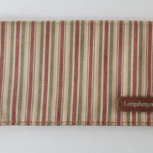 May include: Folded rectangular fabric item with vertical stripes in beige, red, and green. A brown leather tag with the brand name "Longaberger" is attached. The item is likely a wallet or similar accessory.
