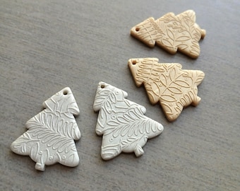 May include: Four Christmas tree-shaped ornaments with detailed leaf and floral patterns. Two are off-white, and two are tan. Each has a small hole at the top for hanging. The ornaments are arranged on a gray surface.
