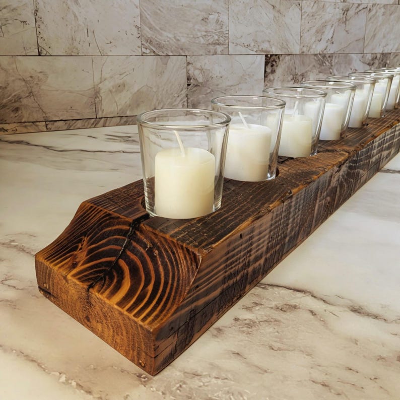 May include: A rustic, wooden candle holder with a dark brown finish. It features a series of clear glass votive holders, each containing a white candle. The design is simple and elegant, perfect for home decor.
