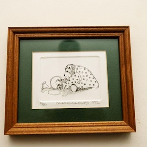 May include: A framed pen and ink drawing featuring a bear playing a horn. The bear is wearing a polka-dotted coat. The artwork is set against a green mat and framed in a brown wooden frame. The text "CALLING ALL BEARS" is visible.