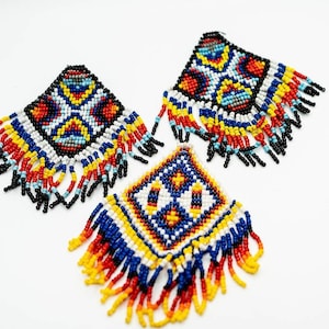 Peut inclure: Trois ornements carrés perlés avec des motifs géométriques colorés. Les motifs présentent des perles rouges, jaunes, bleues et blanches, avec des franges noires le long des bords inférieurs. Les ornements sont sur fond blanc.