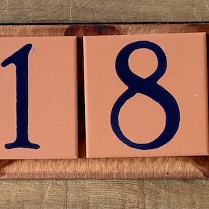 May include: A wooden address sign featuring six tiles. The first tile has a white and blue floral design. The following tiles display the numbers 4, 1, 8, 5, and 6 in navy blue. The tiles are set on a brown wooden base.