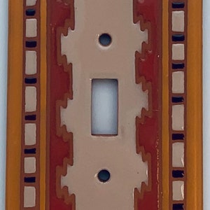 May include: A ceramic light switch cover with a Southwestern design. The cover features a beige background with red, orange, and black geometric patterns.