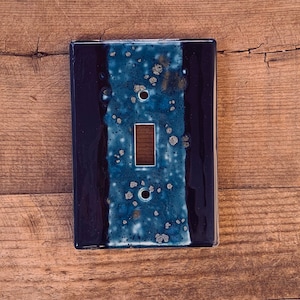 May include: A blue and black ceramic light switch cover with a speckled design. The switch cover has a single switch opening.
