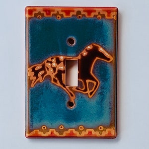 May include: A ceramic light switch cover with a turquoise background and a brown horse design. The horse has a white and brown spotted pattern. The cover has a red and gold border with a geometric pattern.