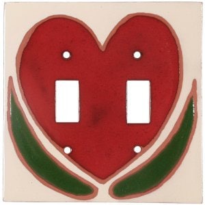 May include: A white ceramic light switch cover with a red heart design and green leaves. The heart has two light switch openings.