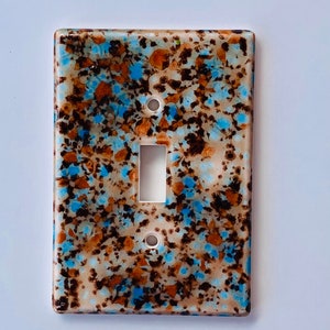 May include: A ceramic light switch cover with a speckled pattern in shades of brown, blue, and white.