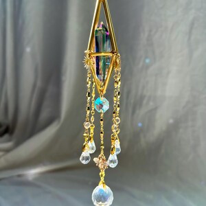 May include: A gold geometric pendant necklace with a iridescent crystal prism and a dangling crystal drop. The pendant is suspended from a delicate gold chain.