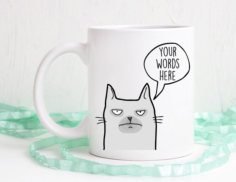 A custom mug with words that go in a speech bubble above a grey cat. The cat looks displeased.