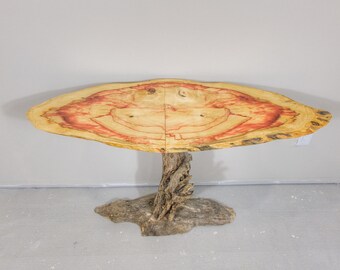 May include: A unique, handcrafted wooden table. The tabletop is a light brown color with red and orange accents, supported by a natural wood base. The table's design highlights the natural grain and texture of the wood.